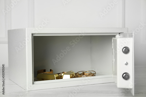 Open steel safe with gold bars and jewelry on wooden table