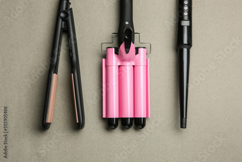 Set of modern hair irons on grey background, flat lay photo
