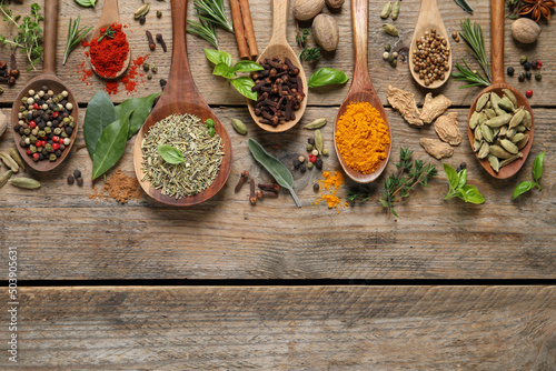 Different herbs and spices with spoons on wooden table  flat lay. Space for text