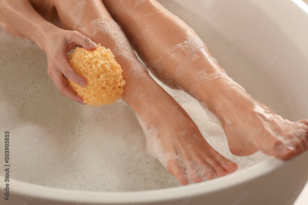 Fototapeta premium Woman rubbing her leg with sponge while taking bath, closeup