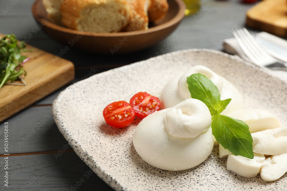 Delicious burrata cheese with basil and cut tomato on grey wooden table, closeup