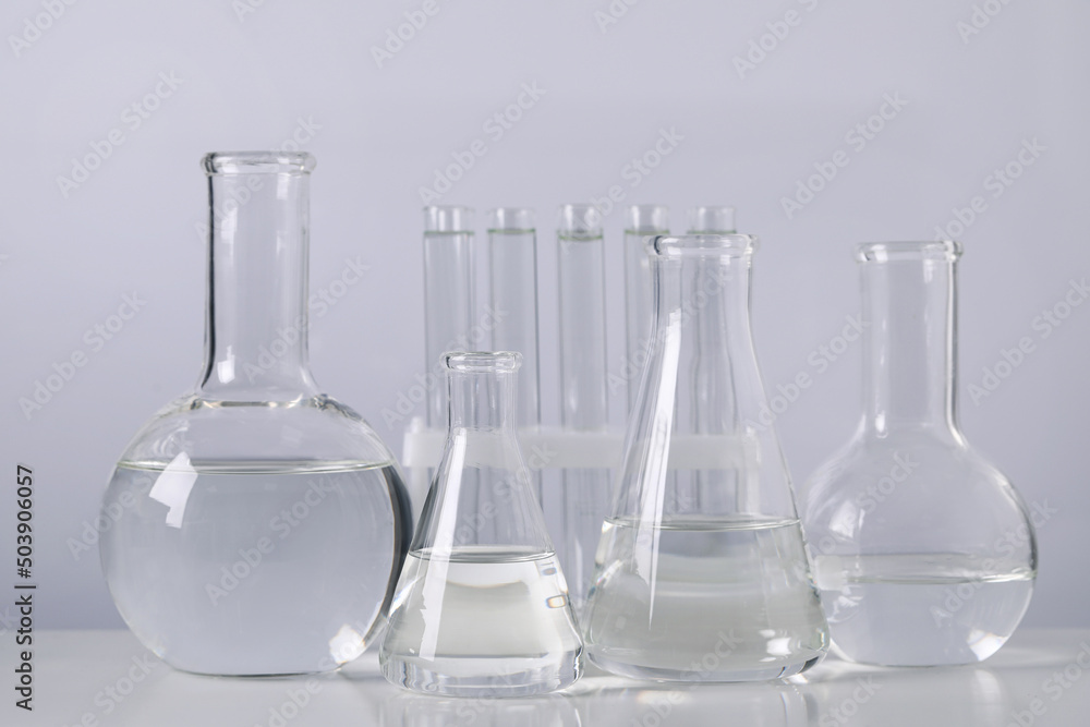 Different laboratory glassware with transparent liquid on table against light background Different laboratory glassware with transparent liquid on table against light background