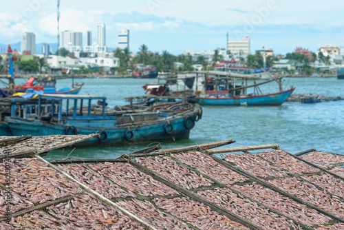 Traditional drying of salted fish on racks against the background of fishing boats and city of Nha Trang, Vietnam.