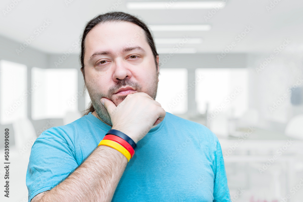 Φωτογραφία An adult, unshaven man in a T-shirt holds his chin thoughtfully