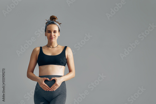 Pregnant woman holding her hands in a heart shape on her belly. Pregnant belly with fingers heart symbol. Maternity, motherhood, pregnancy, happiness concept