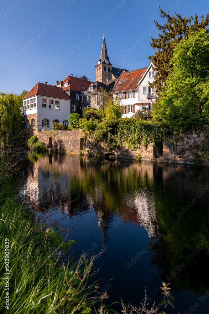 Old town of Essen-Kettwig Ruhr Basin Germany reflected in water of mill ditch. The small historic village with romantic truss houses and Market Church is a tourist attraction. Blue sky in springtime.