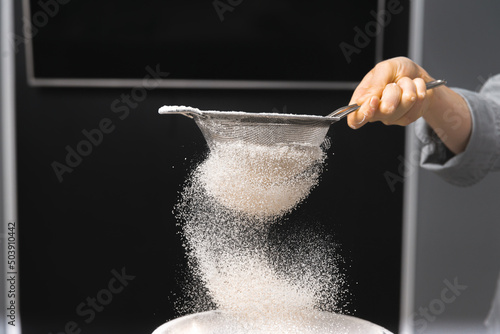 Close up photo of a human hand sieving flour and getting ready for baking over dark background. photo