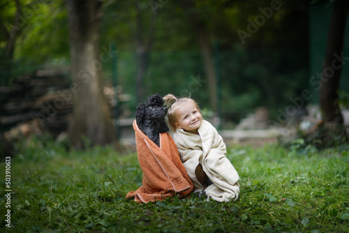 Cute baby toddler in towels with pet. Child and black poodle in a towel after swimming in the backyard in summer