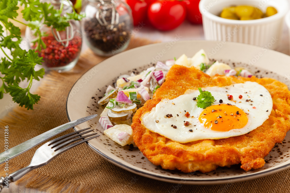 Viennese pork schnitzel with a fried egg. Served on potato salad. Natural wooden planks in the background.