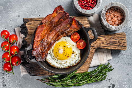 English breakfast with fried egg and bacon in cast iron pan. Gray background. Top view