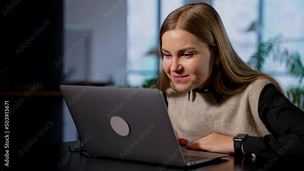 Resilient smiling woman working on computer pulls closer to the screen. Lady rejoicing looking at her laptop rising hands cheerfully. Resilient smiling woman working on computer pulls closer to the screen. Lady rejoicing looking at her laptop rising hands cheerfully.