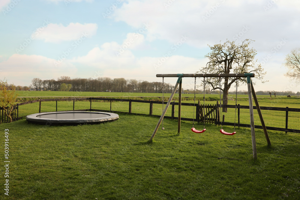 Wooden swings and trampoline on green lawn outdoors