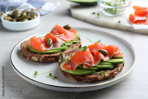 Delicious sandwiches with salmon, avocado and capers on white wooden table