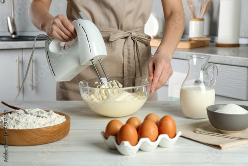 Fototapeta Woman whipping white cream with mixer at light grey table in kitchen, closeup