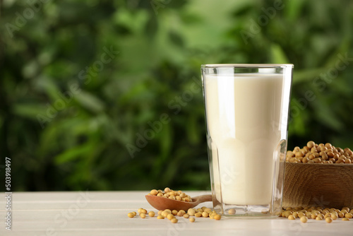 Glass with fresh soy milk and grains on white wooden table against blurred background. Space for text