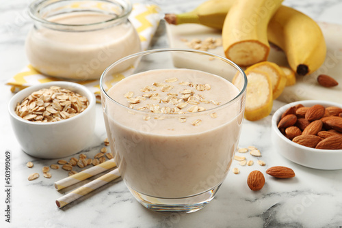 Glass of tasty banana smoothie with oatmeal on white marble table