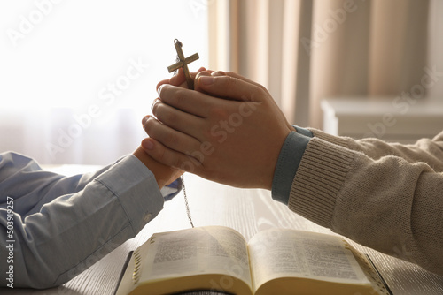 Tableau sur toile Boy and his godparent praying together at white wooden table indoors, closeup