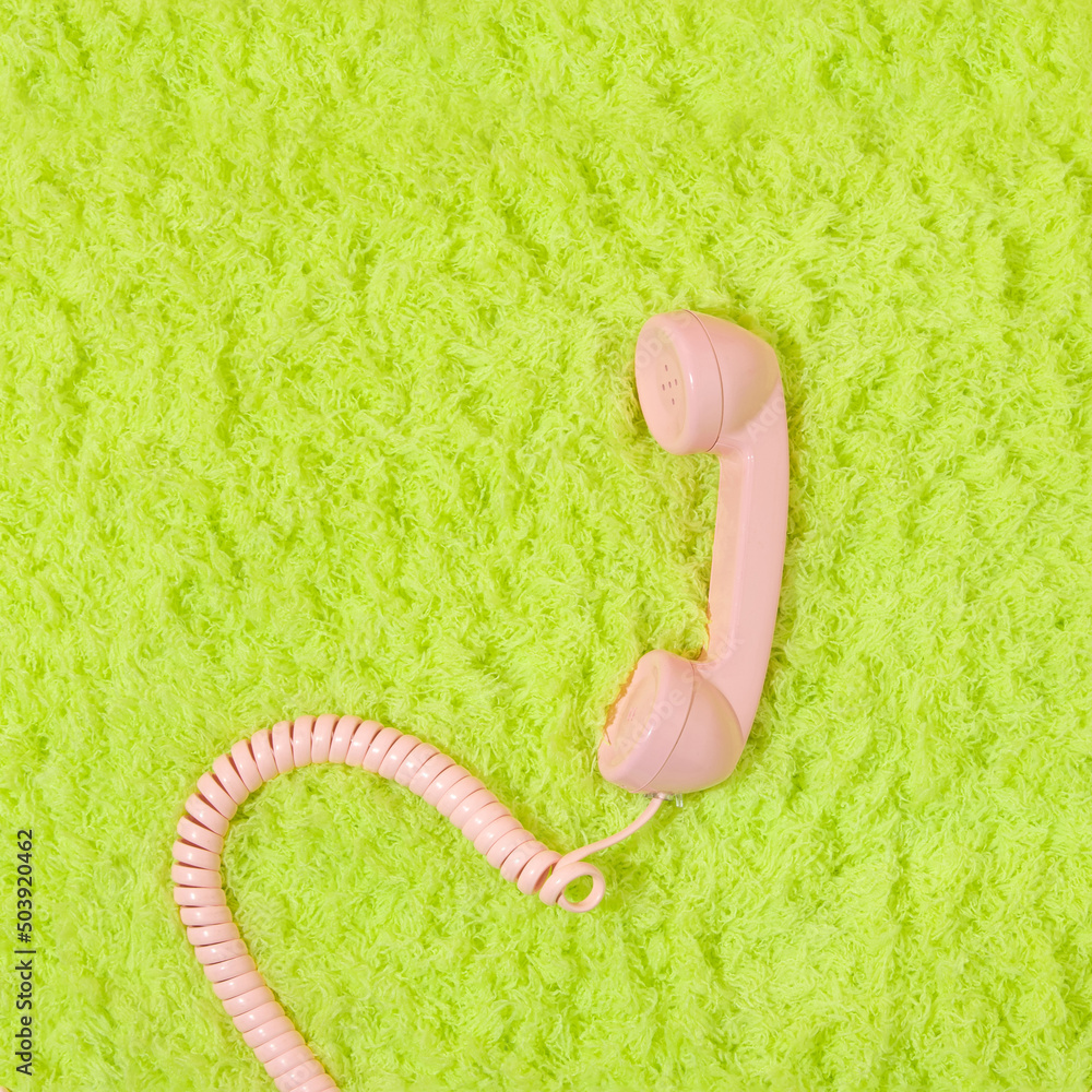 Pastel pink retro telephone handset on neon green fluffy shaggy