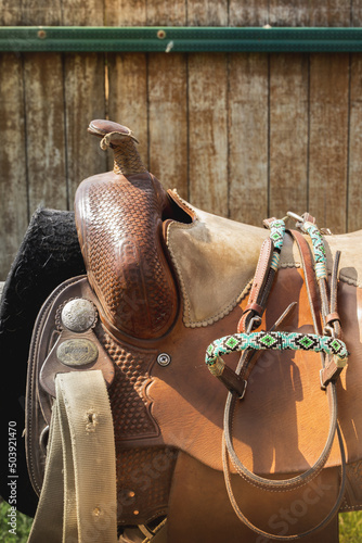 Beautiful leather saddle in the West style. Horse equipment against the background of a wooden paddock fence