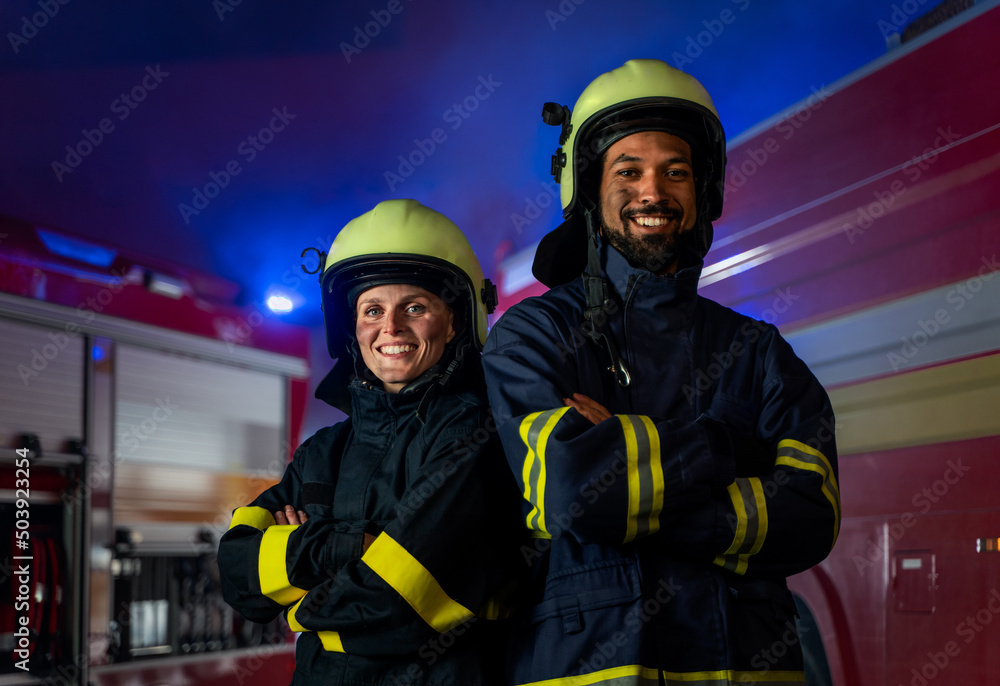 Happy firefighters man and woman after action looking at camera with fire truck in background Happy firefighters man and woman after action looking at camera with fire truck in background