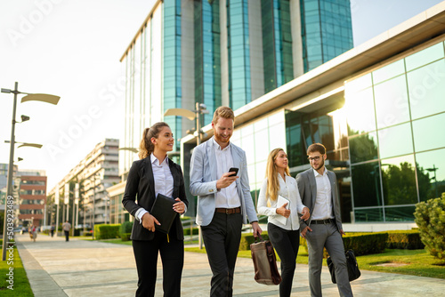 Group of cheerful young business people talking to each other while walking outdoors photo