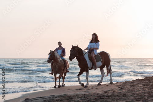 a loving young couple in summer clothes riding a horse on a sandy beach at sunset. Sea and sunset in the background. Selective focus 