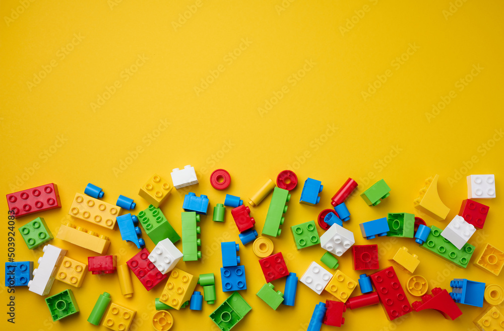 Scattered parts of a plastic children's designer, top view. Yellow background