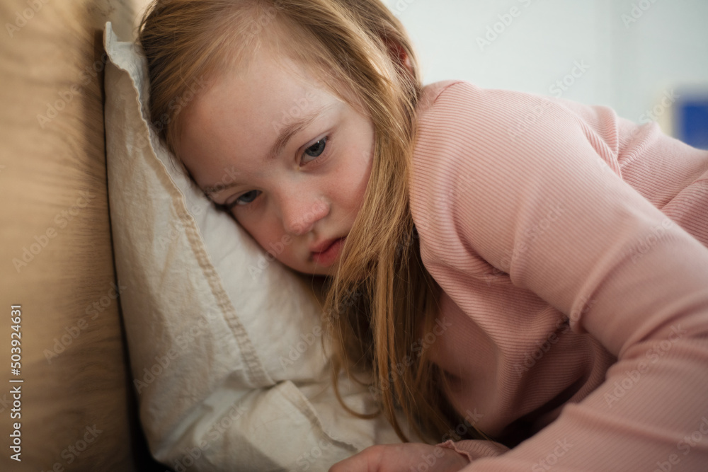 Fototapeta premium Sad little girl with Down syndrome lying on bed at home.