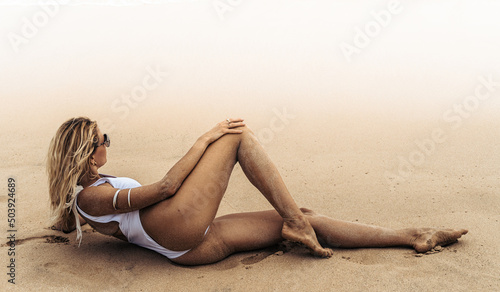 Modelka w białym kostiumie kąpielowym na tropikalnej plaży na tle oceanu. photo