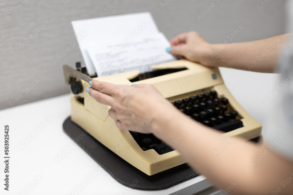woman typing on a typewriter presses the carriage return lever - obrazy, fototapety, plakaty 