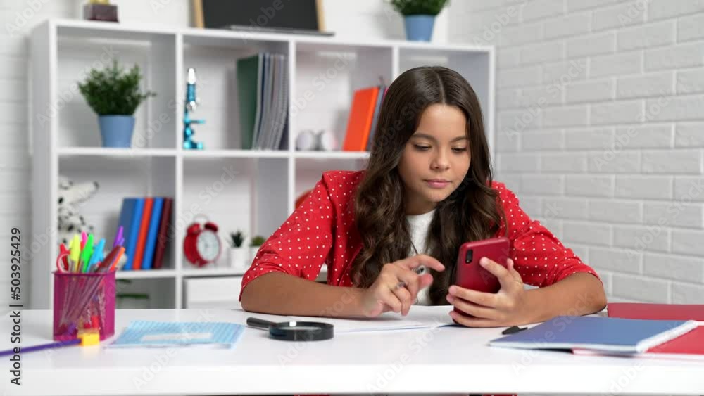 Serious girl child doing homework using mobile phone at school desk, smartphone learning Serious girl child doing homework using mobile phone at school desk, smartphone learning