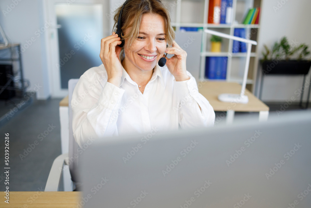 Laughing businesswoman wearing headset talking to caller in customer services department