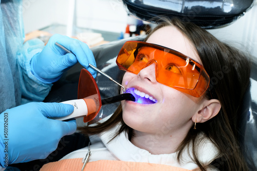 Portrait of a girl in dentistry. The hands of the dentist hold the tools and treat the teeth of the girl. Close-up. The girl is wearing orange goggles.