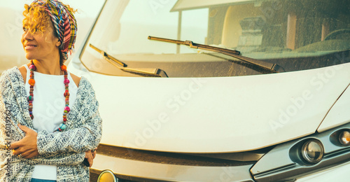 Happy mature woman smile and enjoy travel lifestyle standing against a big modern white motorhome. Sunlight in background. Happy travel and tourism concept. Independent female people and freedom