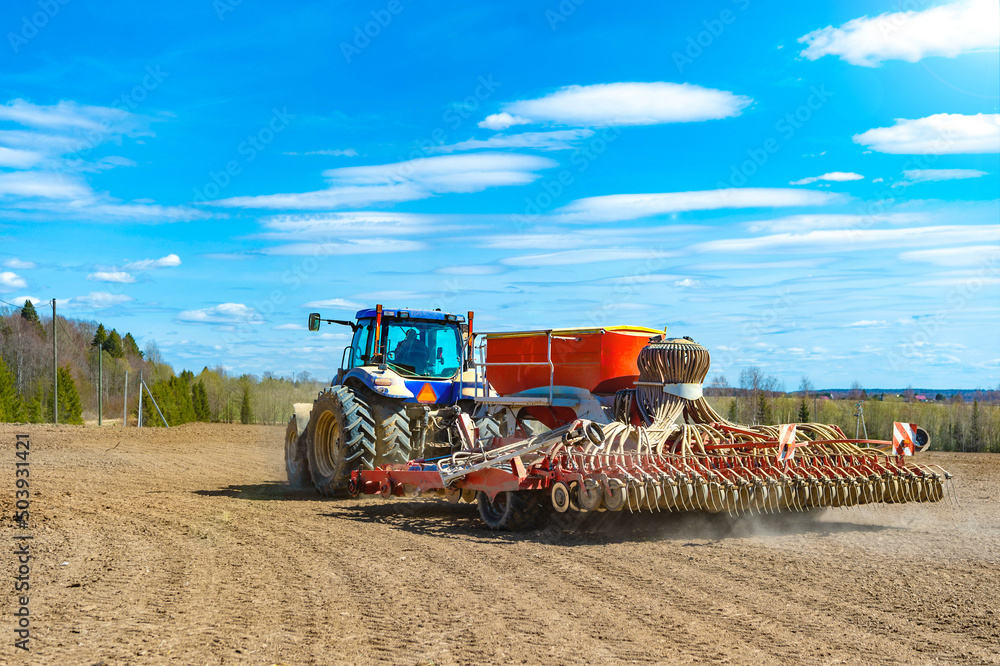 Obraz premium A tractor with a seeder in the field sows grains of wheat or oats to grow grain products.Rear view...
