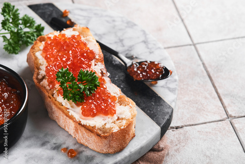 Red caviar sandwiches. Salmon red caviar in bowl and sandwiches on marble plate on old gray cracked tile table background. Top view. Copy space.
