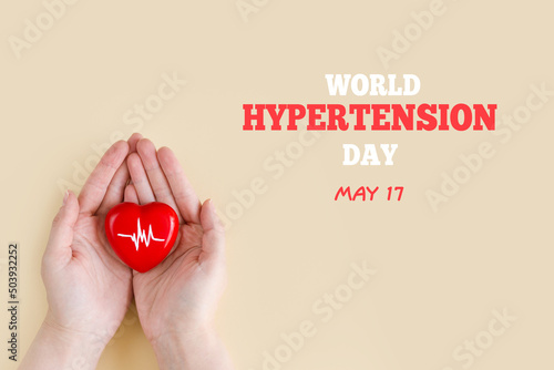 World Hypertension Day. Women's hands hold red heart with heartbeat chart - a symbol of high blood pressure. Hypertension Day in May 17th. World heart day