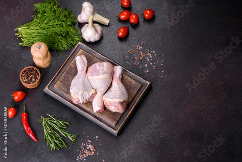 Three legs of raw chicken with spices and herbs on a wooden cutting board
