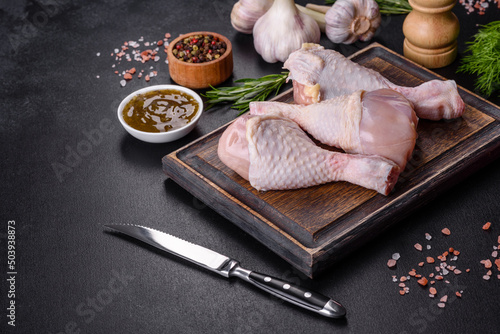 Three legs of raw chicken with spices and herbs on a wooden cutting board
