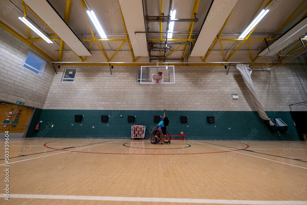 Teenage girl in wheelchair practicing basketball