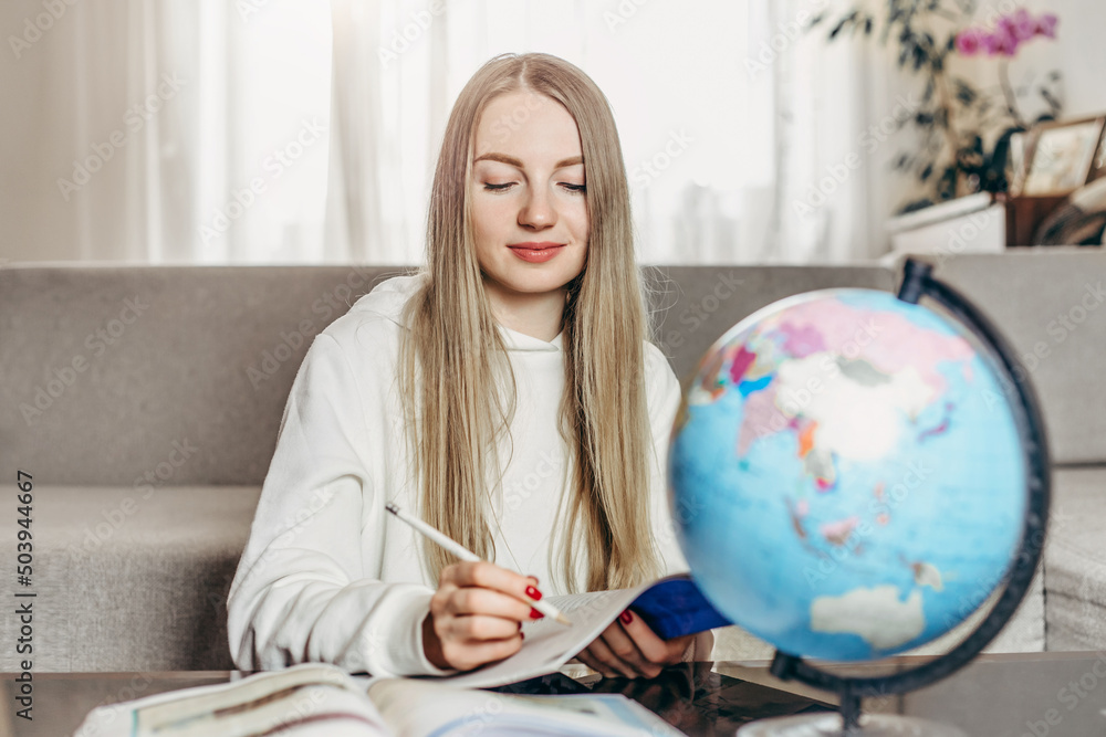 Fototapeta premium Distance learning at home. Young student girl doing homework and preparing for online geography exam
