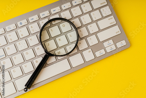 Magnifying glass on computer keyboard on a yellow background