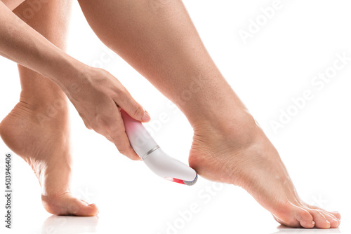 Photos Female feet and electric foot file for callus and dead skin removal on white bac