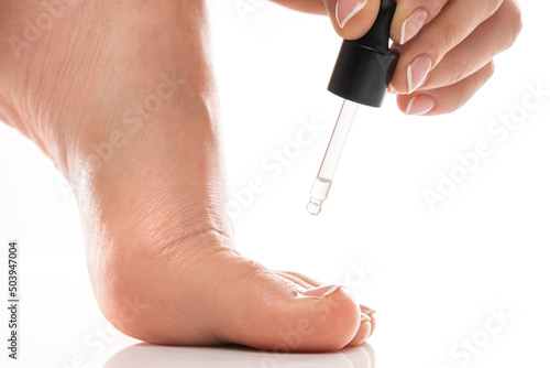 Фотография Closeup of female foot and bottle of nourishing cuticle oil with dropper