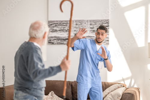 Canvas Print Aggressive patient brandishing his cane at a scared in-home nurse