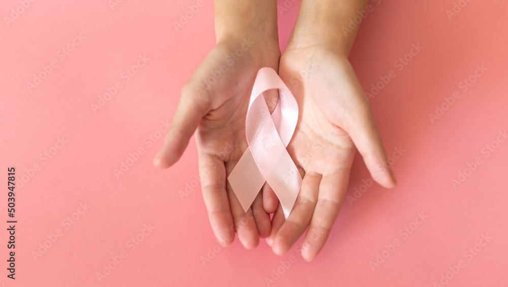 Hands holding pink ribbon on pink background, Breast cancer awareness and October Pink day, world cancer day, national cancer survivor day