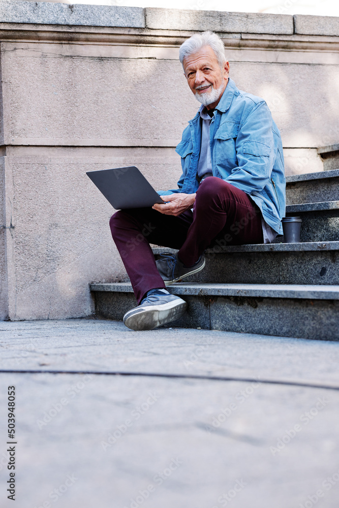A senior student sits on the stairs of the university building and uses his laptop to look at notes before an exam.