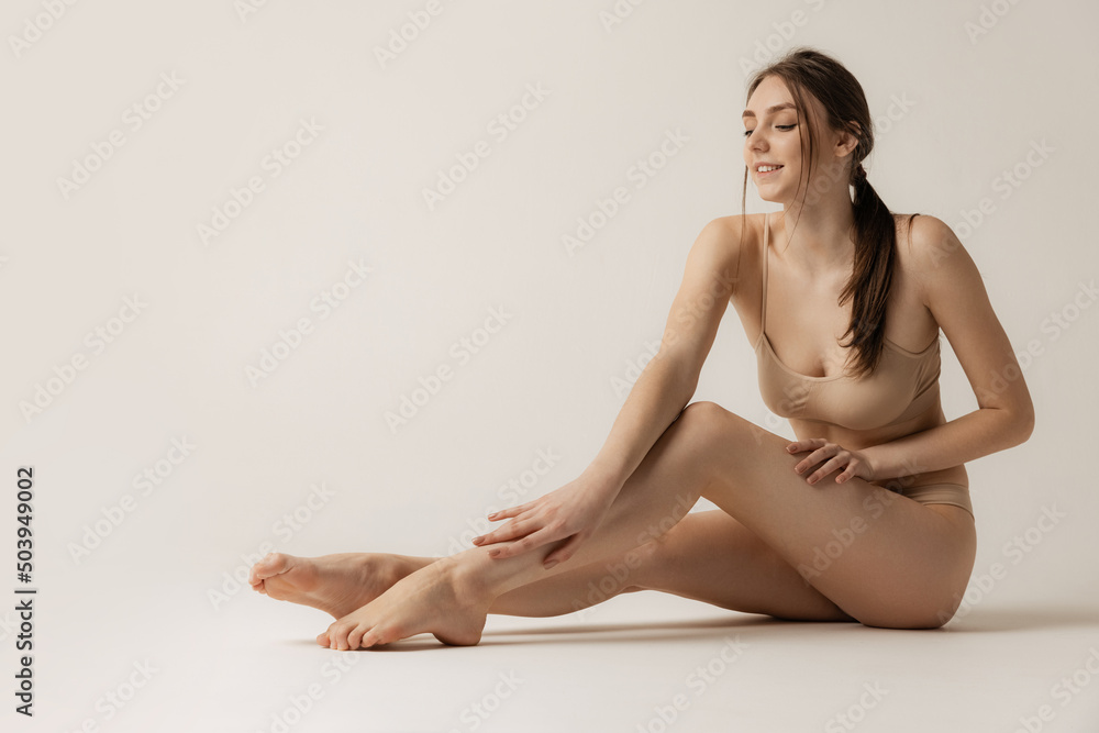 Portrait of young woman in beige underwear isolated over grey studio background. Taking care after legs Portrait of young woman in beige underwear isolated over grey studio background. Taking care after legs