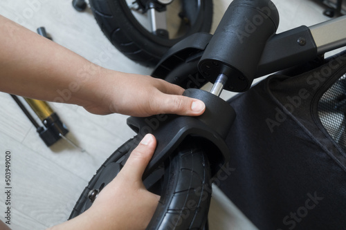 A woman mounts a wheel on a new baby stroller. The process of repairing the assembly of the stroller for a newborn baby. Carriage wheel assembly. Selective focus