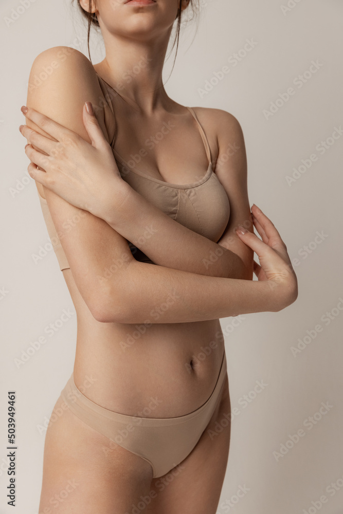 Tender beauty. Young slim woman posing in beige underwear isolated over grey studio background